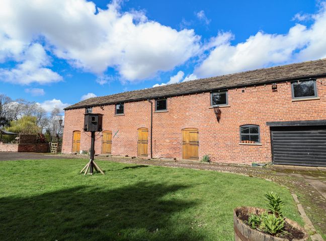 A brick building with wooden doors and a birdhouse on a grassy lawn at Lake View Barn in Henbury Macclesfield