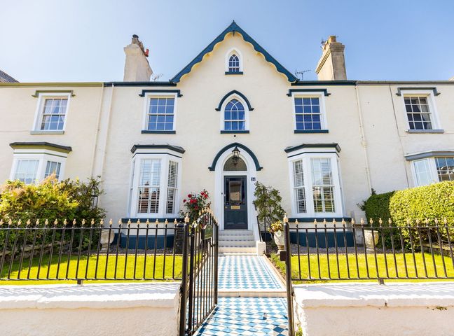 The exterior of a white house with blue trim a tiled pathway a black iron gate and green lawn at Abbey Lodge in Llandudno