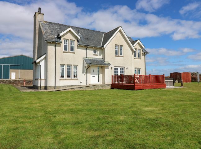 A two-story house with multiple windows and a red wooden deck in a large grass lawn at Drummygar Mains in Arbroath