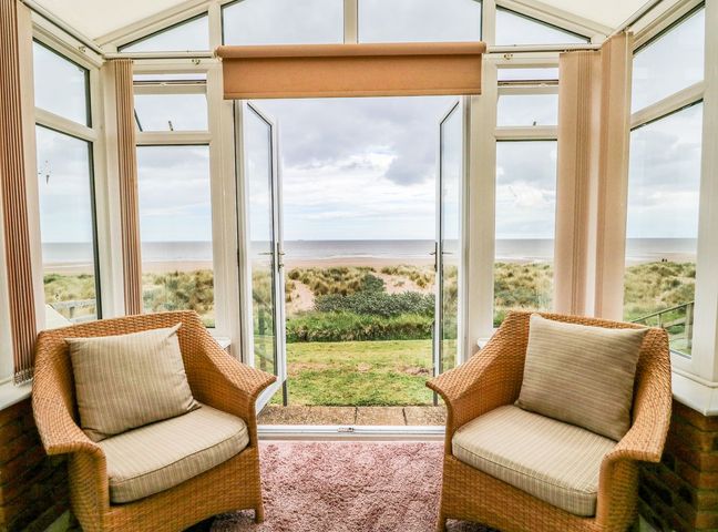 A sunroom with two wicker chairs facing the sea at Windyridge in Anderby Creek near Chapel St Leonards