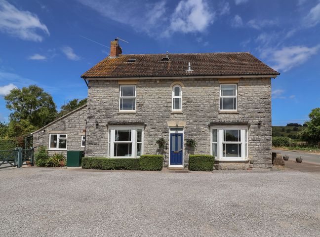 A stone house with a blue door and bay windows by a gravel driveway at Metcalfe House in Compton Dundon