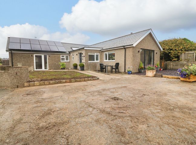 A single-story house with solar panels on the roof a small garden area and outdoor chairs at Terfyn Bach in Morfa Nefyn