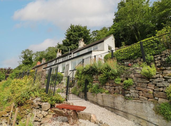 A hillside house with a stone retaining wall and metal fence surrounded by greenery at Roseville in Cromford