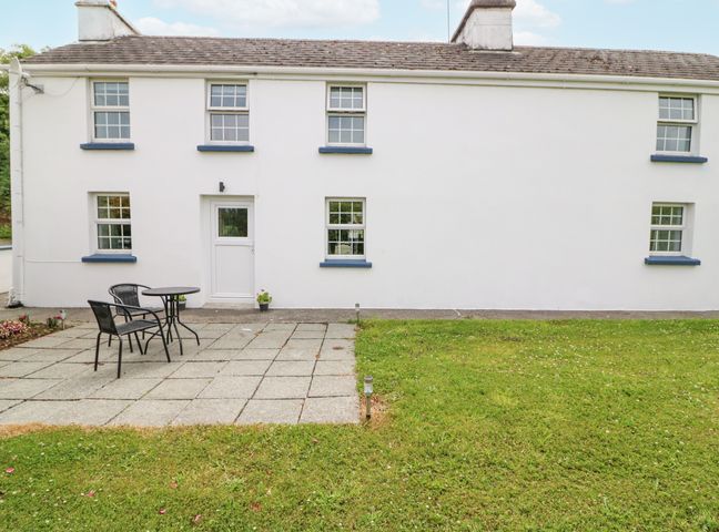 A white house with blue window sills and a small patio with table and two chairs at Aunties in Ballylickey County Cork