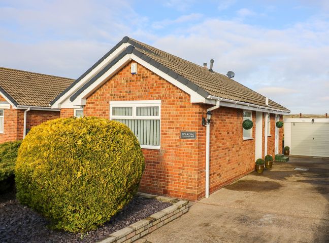 A brick house with a large rounded bush in front and a driveway leading to a garage at Sea Roke in Filey