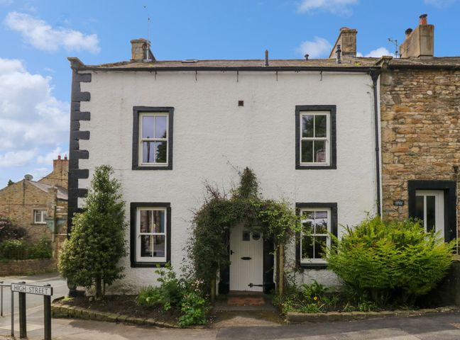 A white two-story house with black window frames and a door covered with greenery on a street corner at Burton House in Burton-In-Lonsdale