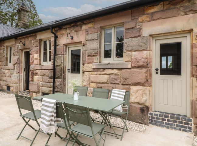 An outdoor patio with a green table and chairs against a stone building wall at Hazel Cottage - Fold Yards in Alderwasley near Crich