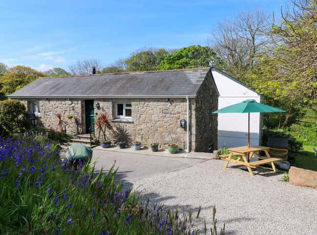 A stone cottage with potted plants and a picnic table with green umbrella in the garden at Chy-An-Oula Seworgan near Constantine