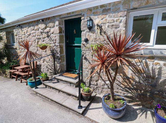 Stone exterior wall with green door steps potted plants and a wooden bench at Chy-An-Oula in Seworgan near Constantine
