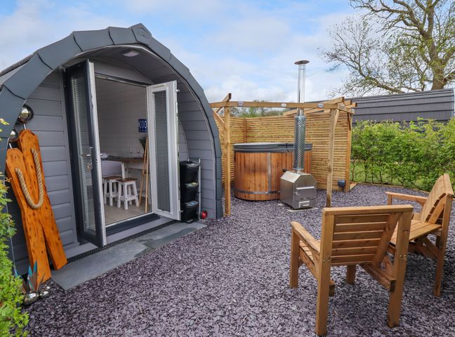 An outdoor area with two wooden chairs a wooden hot tub a gray pod-shaped cabin with open doors at Moel Famau Bryniau Clwyd near Denbigh