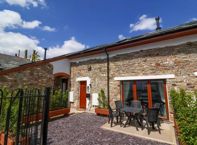 An outdoor patio with a table and chairs outside a stone building at Bumblebee Meadows in Parkham near Bideford