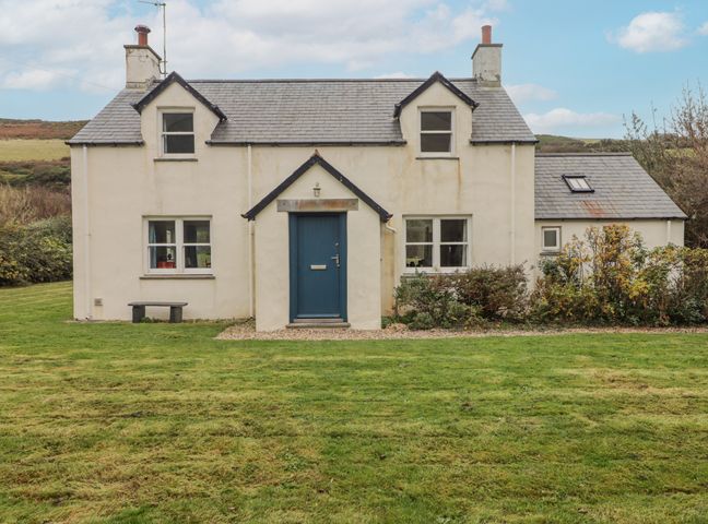 A two-story house with a blue door and grass lawn at Ger Y Traeth in Pwllgwaelod near Dinas Cross