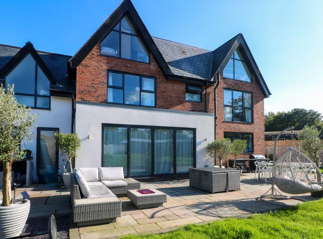 An outdoor patio area with wicker furniture and a hanging chair outside a modern brick house at Rye Croft in Willaston near Neston