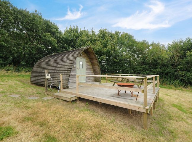 A wooden pod structure with a deck table and fire pit on a raised wooden platform at Sheep Shed Penbugle Organic Farm in St Keyne near Looe