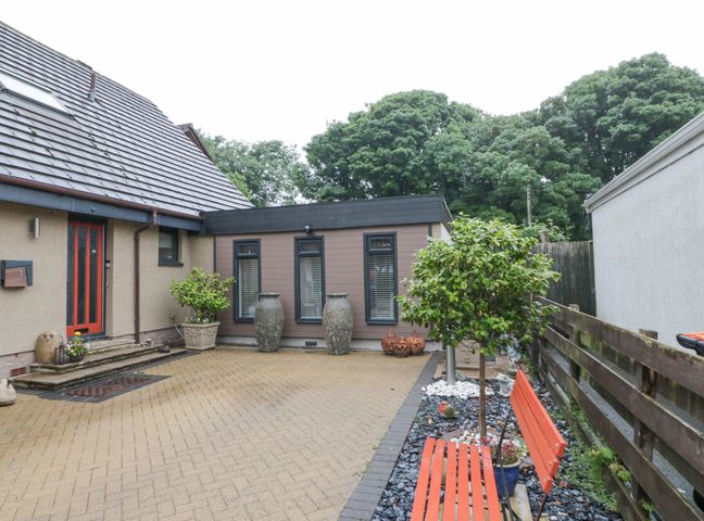 A paved yard with red bench and potted plants outside a house at Scotia At The Pow in Powfoot near Annan