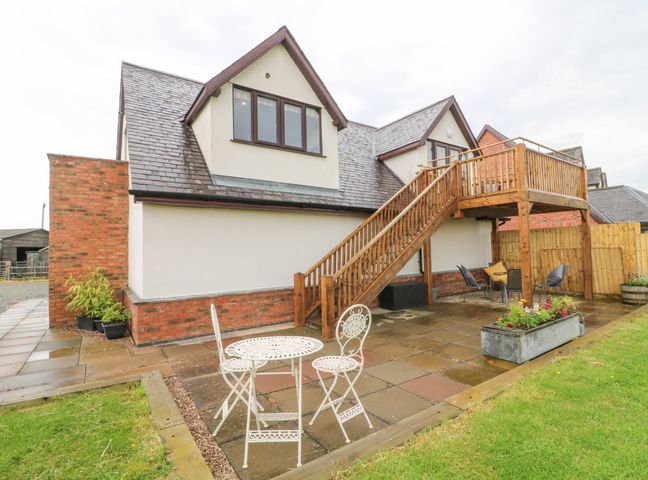 A patio with a white metal table and chairs wooden stairs leading to a balcony and a seating area at Fourways Loft in Smeeton Westerby near Kibworth