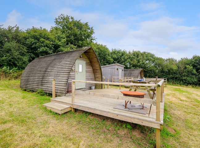 Wooden pods with a deck and picnic tables in a grassy area surrounded by trees at Hen House @ Penbugle Organic Farm in St Keyne near Duloe