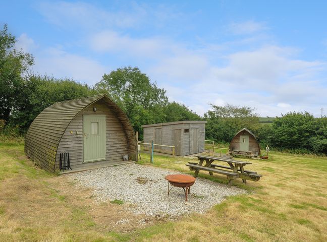 An outdoor area with wooden cabins a picnic table and a fire pit at Pig Pen @ Penbugle Organic Farm in St Keyne near Duloe