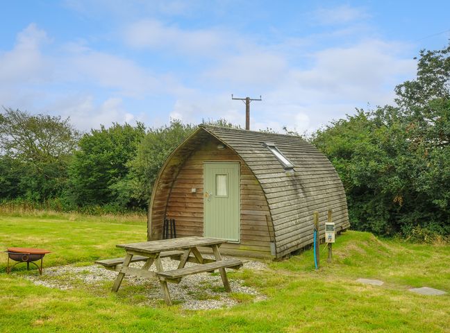 A wooden pod cabin with a green door and picnic table outside in a grassy area at Fox Den @ Penbugle Organic Farm in St. Keyne near Duloe