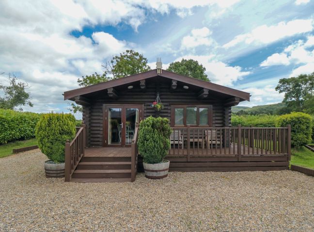 The front exterior of a wooden lodge with a small deck and steps surrounded by greenery at Endeavour Lodge 4 in Stokesley