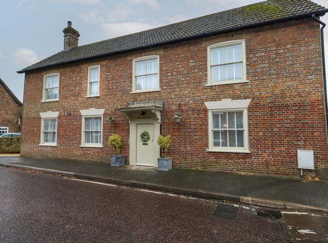 A brick house with six windows and a central door with plants on the pavement at Manor Farm House in Bere Regis