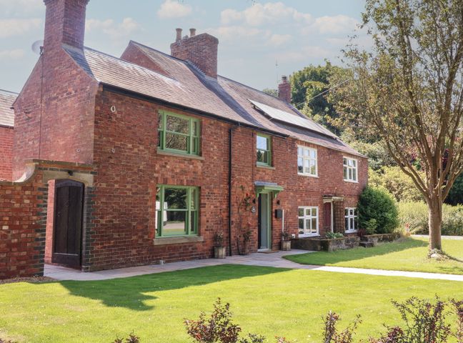 A brick house with green window frames and a tree in the lawn at Rose Cottage in Langham near Oakham