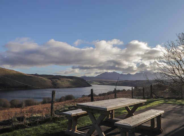 A table and benches by the water with mountains in the distance at Arnaval in Carbost