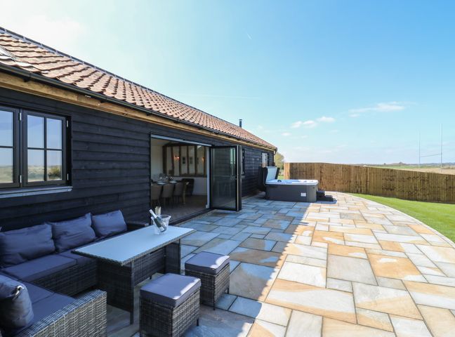 An outdoor patio with a sectional sofa a table stools and a hot tub at The Hide in Mersea Island