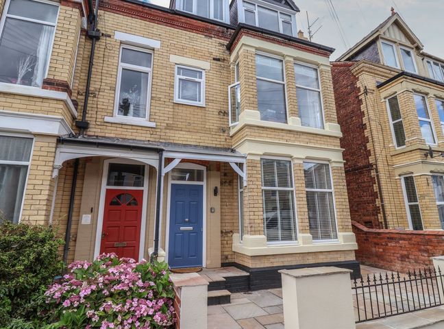 A front view of a two storey townhouse with a blue door and a red door with a flowering bush in front at Coral Villa in Bridlington