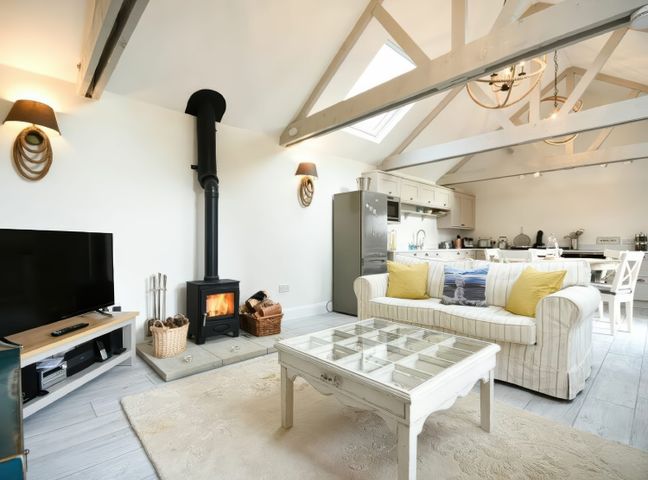An open living space with a sofa yellow cushions coffee table and wood burning stove at East Farm Croft in Embleton