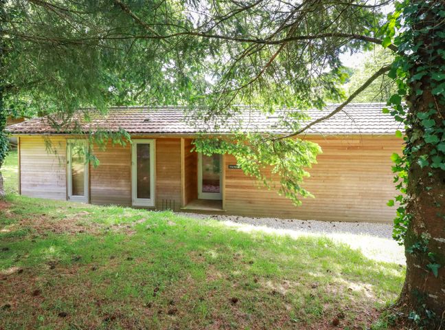 A wooden house with three glass doors surrounded by trees and grass at 10 Waters Edge in Lanreath
