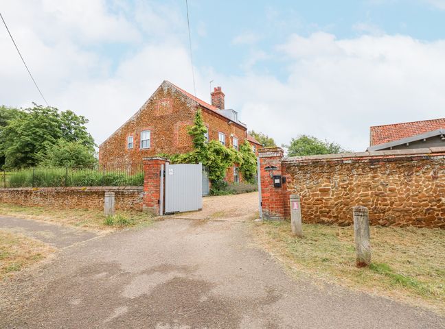 A view of a brick house behind a stone wall and open gate with a driveway at Malthouse Farm in Heacham