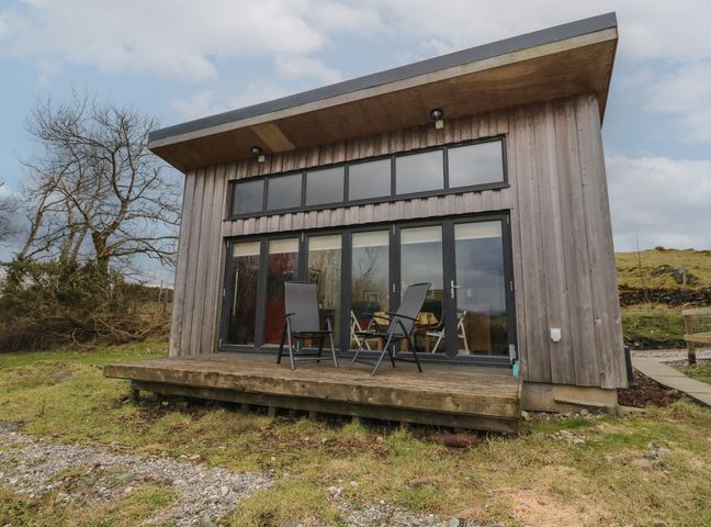 A wooden cabin with glass doors and two chairs on a deck in a grassy area at Tirlaggan Studio in Lismore