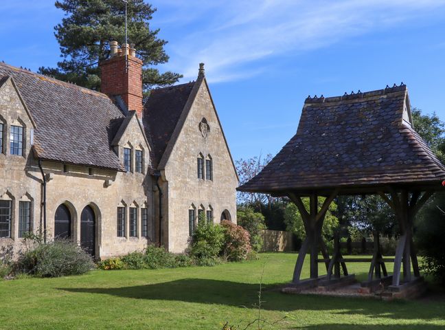 A stone house with a tiled roof and black windows next to a wooden structure with a tiled roof in a garden at The Alms House East in Forthampton near Tewkesbury