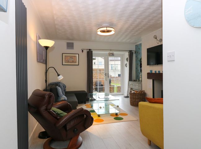 A living room with a brown recliner chair a gray sofa a glass coffee table and double doors to a garden at 101a Pettycur Road in Kinghorn