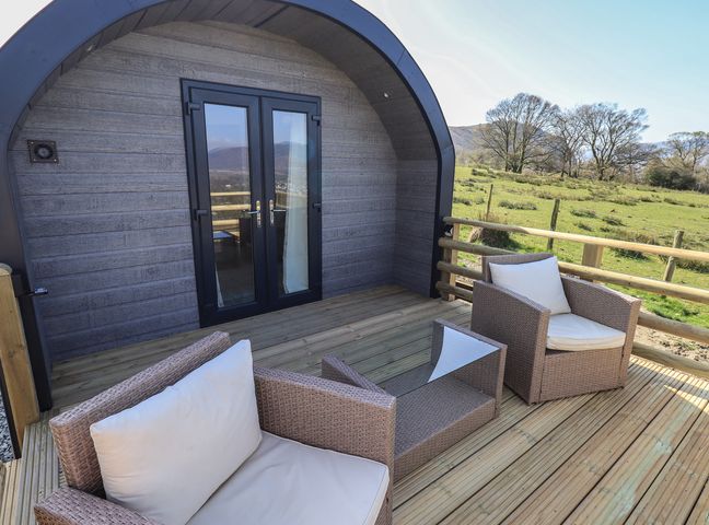 A wooden deck with two cushioned chairs and a small table outside a curved cabin at Shepherds View in Castlerigg near Keswick