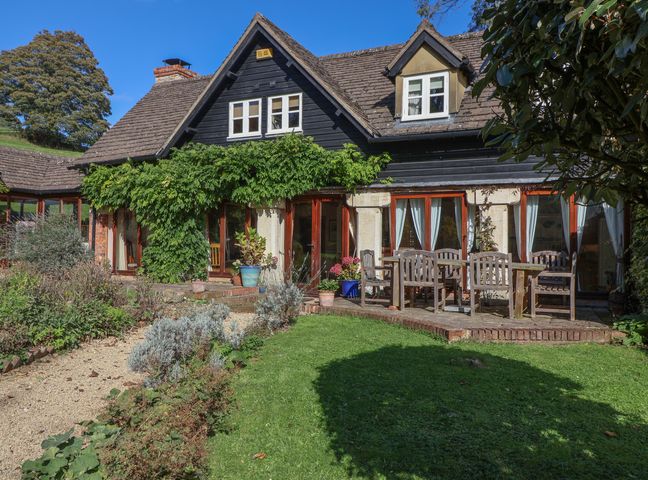 A house with a garden patio and outdoor wooden table and chairs at Highgrove Barn in Painswick
