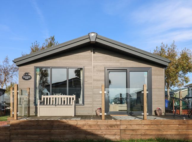 A wooden lodge with glass doors and windows a bench on the deck and trees around Brocklebank Lodge 35 in High Hesket near Armathwaite