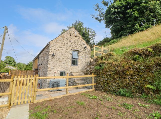 A stone building with a wooden fence and gate near a grassy slope at Horsedale Barn in Bonsall