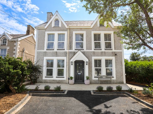 A two-story house with multiple windows a black front door and a paved driveway with plants at Highways in Morfa Nefyn