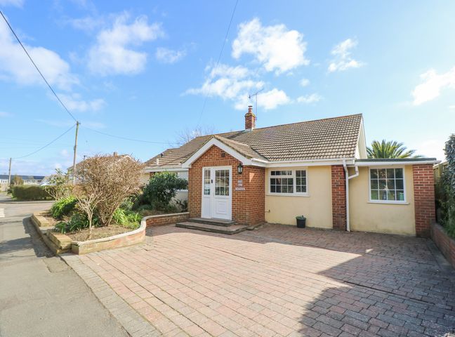 A single story house with a brick and beige exterior and a tiled roof with a paved driveway and a small garden bed at Bay Cottage in Bembridge