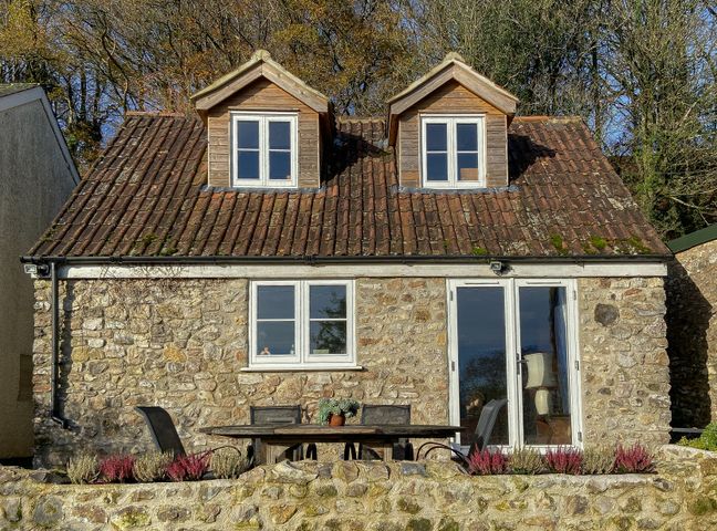 A stone house with two dormer windows a patio table and chairs in front at The Wheelhouse in Beacon near Yarcombe