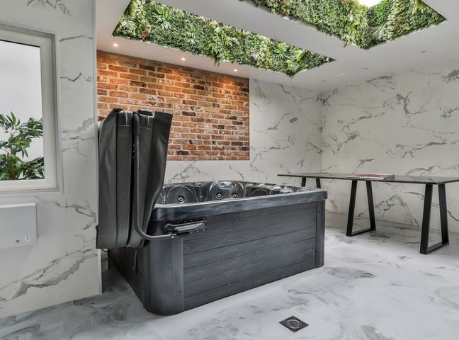 An indoor room with a hot tub a table and a wall with brick and marble patterns and a ceiling with plants at 23 Trafalgar Square in Scarborough