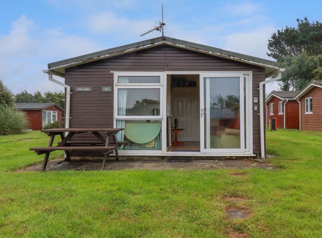 A small brown cottage with a sliding glass door and a picnic table on the grass at Fox Cove near St Merryn