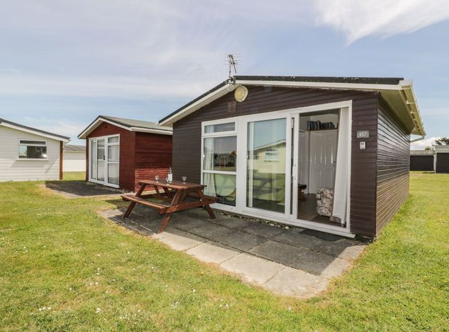 A small wooden cabin with sliding glass doors and a picnic table outside on a grassy area at Warren Cove near St Merryn