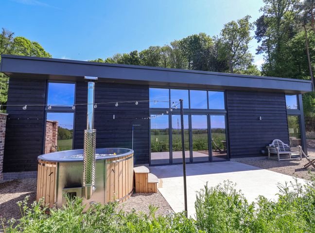 A modern building with large glass windows a wooden hot tub and outdoor seating at Brock House in Cotcliffe Bank Farm near Northallerton