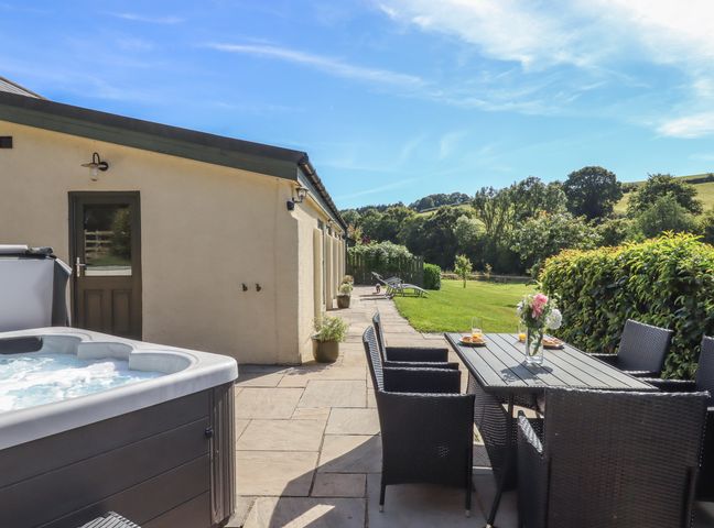 An outdoor patio with a hot tub dining table and chairs overlooking a garden at Binneford Barn Kennerleigh near Cheriton Fitzpaine