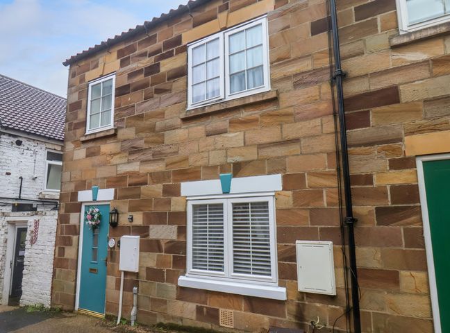 The exterior of a brick house with a teal door and two white-framed windows at 1 Johnson's Yard in Guisborough