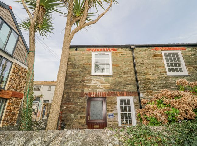 Stone cottage exterior with a wooden door and two white-framed windows small tree and plants in front at Boatmans Cottage in Salcombe
