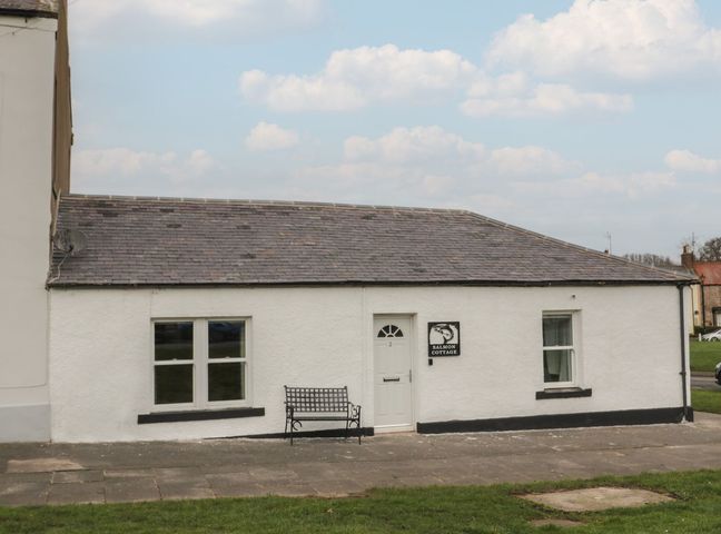A white cottage with a bench outside and a sign that reads Salmon Cottage in Norham